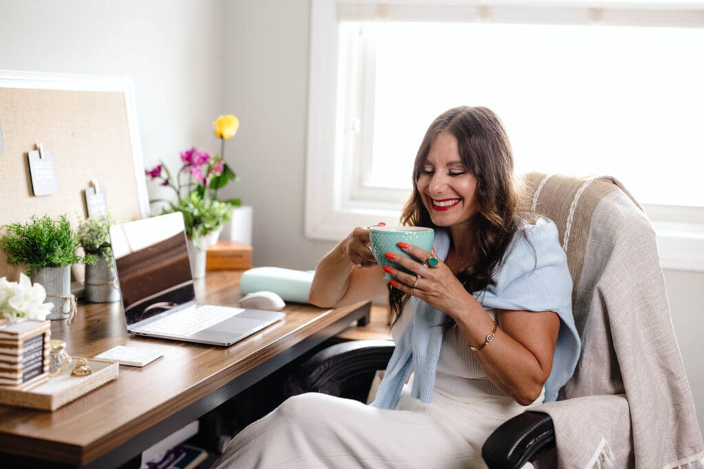 Angela Reina of Reina Smith Media sipping a cup of coffee at her desk.