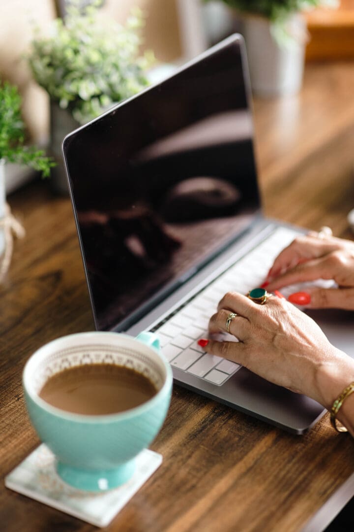 A person is typing on a laptop and drinking coffee.