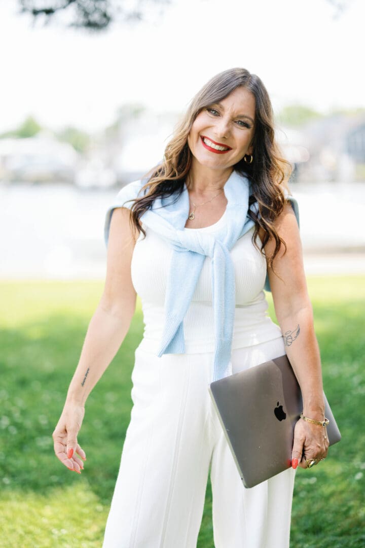 A woman in white dress holding a laptop.